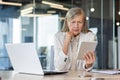 Serious senior gray-haired businesswoman working in office center, sitting at desk with laptop and documents, looking at Royalty Free Stock Photo