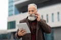 Serious senior man looking at digital tablet, talking on phone Royalty Free Stock Photo