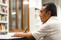 Serious senior man sitting on a library bench, writing in his book. Royalty Free Stock Photo