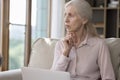 Serious senior woman looks thoughtful while working on laptop