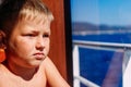 Serious seven-year-old boy looks out the window on the ship