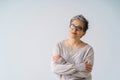 Serious slightly smiling mature grey hair woman in glasses posing with hands folded looking at camera wearing white