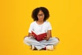 Serious smart teen african american girl in white t-shirt, glasses reading book, sit on floor Royalty Free Stock Photo