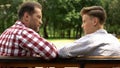 Serious son and dad talking on bench in park, father sharing life experience