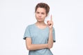 Serious strict young woman looks stressed and pointing up with finger