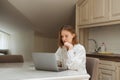 Serious student girl sitting at a table in the kitchen and studying, looking at a laptop screen.Attractive freelance girl working Royalty Free Stock Photo