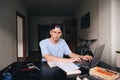 A serious student is studying at home with a laptop in his room sitting at the table. Homework. A look at the camera. Royalty Free Stock Photo