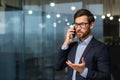 Serious and successful mature businessman inside office near window talking on phone, man in business suit and beard Royalty Free Stock Photo