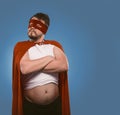 Serious super hero man posing with his arms crossed Confident bearded man in red superhero costume and mask on faded