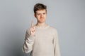 Serious teen boy pointing finger up with confident expression standing over gray background. Young man shaking finger in denial, Royalty Free Stock Photo
