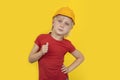 Serious teen boy in protective orange hard hat shows the gesture well done. Child on yellow background Royalty Free Stock Photo