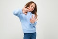 Serious teenage girl in casual blue hoodie refuses crossing her arms in front of herself on a white background with copy