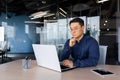 Serious thinking asian businessman working inside modern office, mature man in shirt and glasses using laptop at work Royalty Free Stock Photo