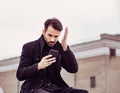 Serious thinking business man in fashion clothing texting sms looking on mobile phone in the hand outdoors autumn background Royalty Free Stock Photo