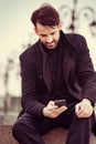 Serious thinking business man in fashion clothing texting sms looking on mobile phone in the hand outdoors autumn background Royalty Free Stock Photo