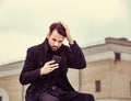 Serious thinking business man in fashion clothing texting sms looking on mobile phone in the hand outdoors autumn background Royalty Free Stock Photo