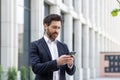 Serious thinking businessman boss holding phone, man reading online message and typing, investor outside office building Royalty Free Stock Photo