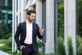 Serious thinking businessman boss holding phone, man reading online message and typing, investor outside office building Royalty Free Stock Photo