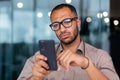 Serious thinking businessman close up, man holding smartphone and reading news online, worker inside office near window Royalty Free Stock Photo