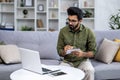 Serious thinking and focused man studying remotely from home, hispanic using laptop to watch online video course and Royalty Free Stock Photo