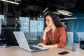 Serious thinking Latin American woman working inside office, businesswoman pondering complex decisions using laptop at