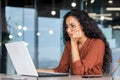 Serious thinking Latin American woman working inside office, businesswoman pondering complex decisions using laptop at