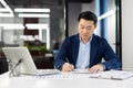 Serious thinking man behind paper work inside office, mature asian man in business suit filling data in table, writing Royalty Free Stock Photo