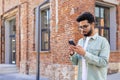 Serious thinking man with phone in hand walking outside office building, young Indian man reading online using Royalty Free Stock Photo