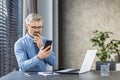 Serious thinking mature gray haired man at workplace inside office, businessman holding phone, thoughtfully reading Royalty Free Stock Photo