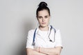 Serious, tired young doctor with a stethoscope in a white coat, standing with arms crossed and looking at the camera Royalty Free Stock Photo