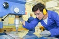 Serious trainees focused on drilling metal piece with professional machinery