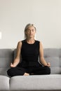 Serious tranquil senior woman meditating at home, keeping zen
