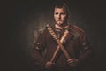 Serious viking with axes in a traditional warrior clothes, posing on a dark background.
