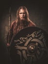 Serious viking with a spear in a traditional warrior clothes, posing on a dark background.