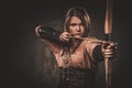 Serious viking woman with bow and arrow in a traditional warrior clothes, posing on a dark background. Royalty Free Stock Photo