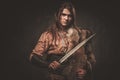 Serious viking woman with sword in a traditional warrior clothes, posing on a dark background. Royalty Free Stock Photo