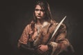 Serious viking woman with sword in a traditional warrior clothes, posing on a dark background.