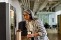 Serious white-haired woman using vending machine while drinking coffee Royalty Free Stock Photo