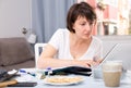 Serious woman with documents using laptop at kitchen table Royalty Free Stock Photo