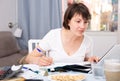 Serious woman with documents using laptop at kitchen table Royalty Free Stock Photo