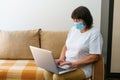 Serious woman in protective mask uses laptop, checks email on internet while Royalty Free Stock Photo