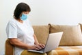 Serious woman in protective mask uses laptop, checks email on internet while Royalty Free Stock Photo