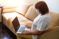 Serious woman in protective mask uses laptop, checks email on internet while Royalty Free Stock Photo