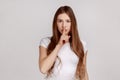 Serious woman showing silence gesture with finger on her mouth, asking to stay quiet, keep secret.