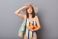 Serious woman wearing swimsuit isolated on gray background standing with oranges keeps hand near forehead looking far waiting her Royalty Free Stock Photo