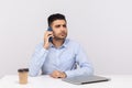 Serious worried businessman sitting in office workplace with laptop, talking on mobile phone, calling partner Royalty Free Stock Photo