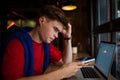 Serious worried man reading text message on mobile phone while sitting with laptop computer Royalty Free Stock Photo