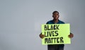 Serious young african american guy in casual clothes looking at camera, holding demonstration banner with BLM text in