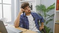 Serious young arab man deep in thought, working on laptop at his office desk, headphones on, fully absorbed in business Royalty Free Stock Photo