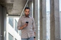 A serious young Arab man in a shirt walks outside an office building and uses a mobile phone intently Royalty Free Stock Photo